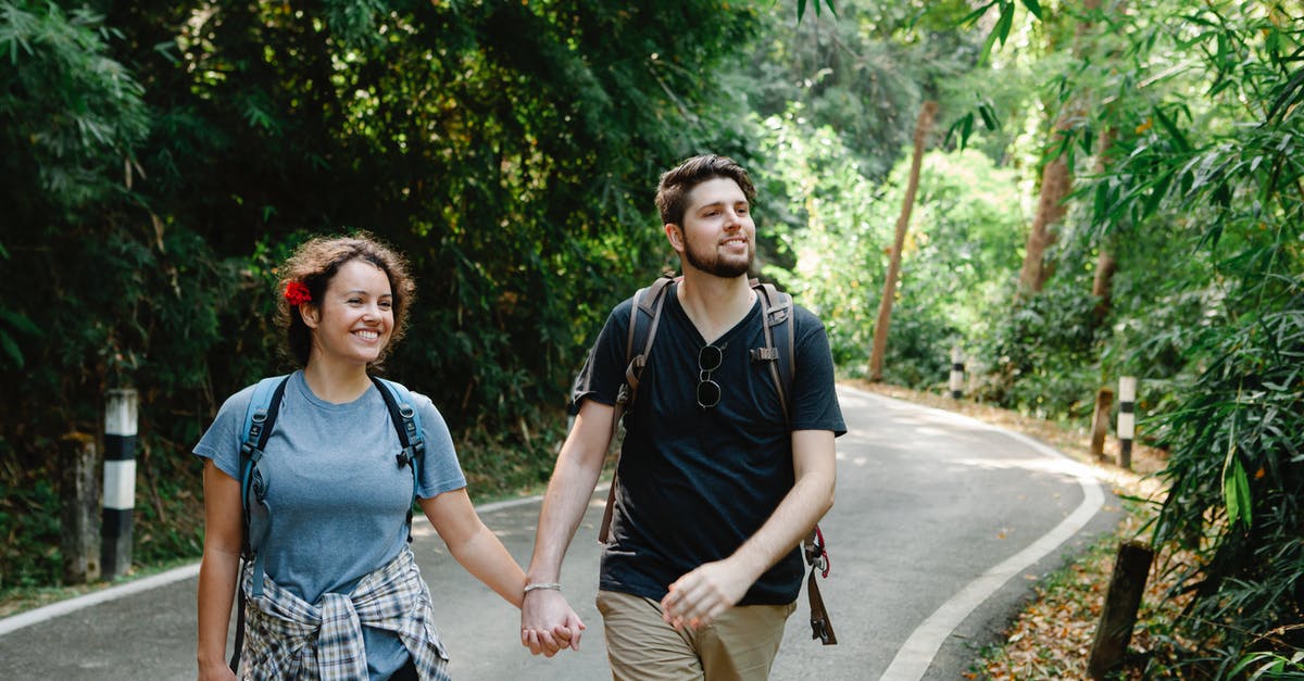 What is the easiest and cheapest way to get a SIM card for a short trip in Mexico? [closed] - Positive loving young couple in casual outfits and backpacks holding hands while strolling on asphalt road between lush tropical trees during hiking in park