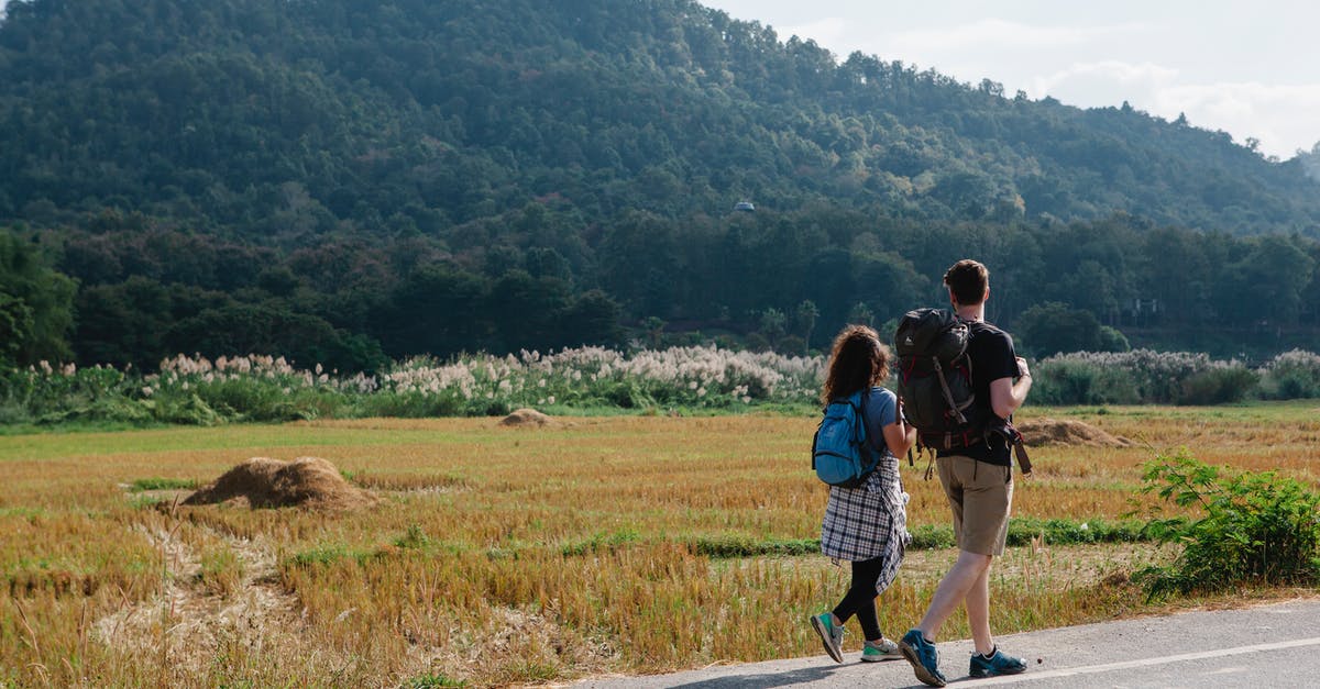 What is the easiest way for my Russian girlfriend to get an EU (Schengen) tourist visa? - Back view of anonymous couple of travelers in casual clothes with backpacks walking along asphalt roadway against green field and hills placed in countryside in sunny day