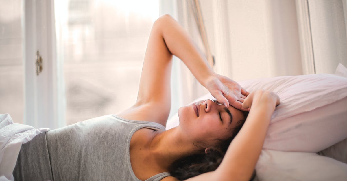 What is the most comfortable way to sleep on a plane? - Woman in Gray Tank Top Lying on Bed What is the most comfortable way to sleep on a plane? - Woman in Gray Tank Top Lying on Bed