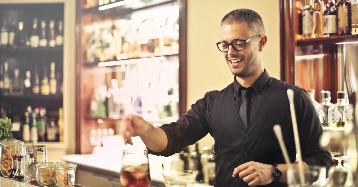 What is the tipping process in restaurants in the US? - Happy young male barkeeper standing at counter and preparing alcohol cocktail for order while working in modern pub What is the tipping process in restaurants in the US? - Happy young male barkeeper standing at counter and preparing alcohol cocktail for order while working in modern pub