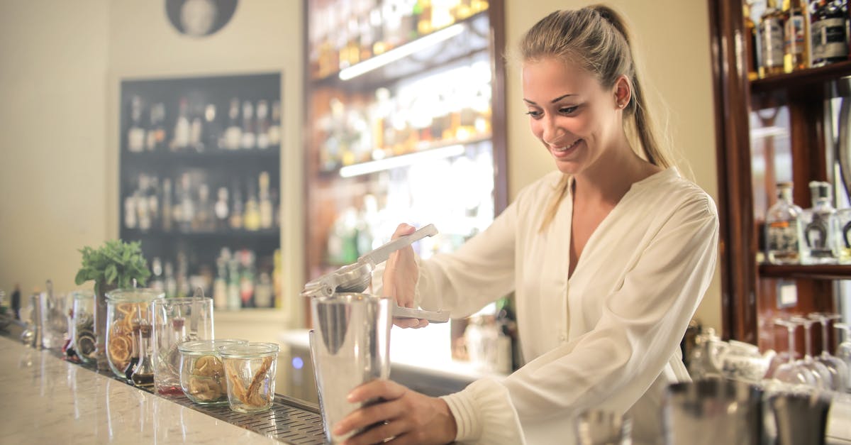 What is the tipping process in restaurants in the US? - Smiling blonde in white blouse squeezing fresh juice into stainless shaker while preparing cocktail in bar What is the tipping process in restaurants in the US? - Smiling blonde in white blouse squeezing fresh juice into stainless shaker while preparing cocktail in bar