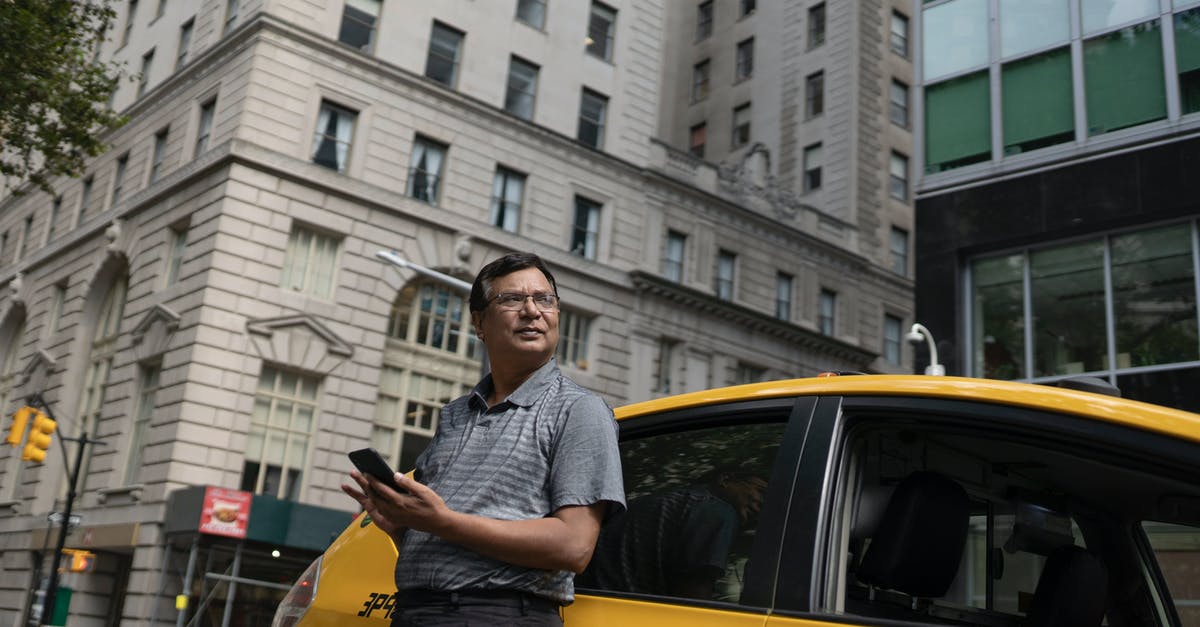 What mobile taxi app can I use in Kutaisi Georgia? - Low angle of serious ethnic male scrolling mobile phone while leaning on yellow car in downtown What mobile taxi app can I use in Kutaisi Georgia? - Low angle of serious ethnic male scrolling mobile phone while leaning on yellow car in downtown