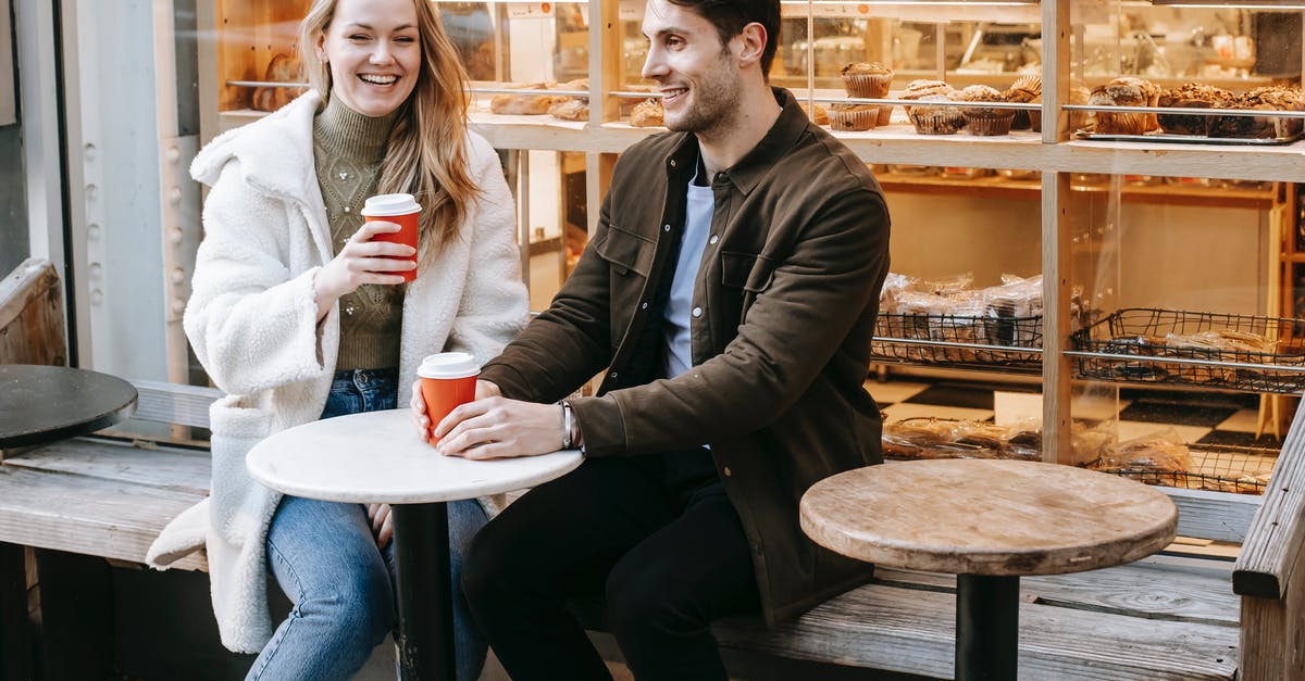 What time do shops close in Taipei? - Cheerful young male and female sitting on wooden bench with takeaway coffee What time do shops close in Taipei? - Cheerful young male and female sitting on wooden bench with takeaway coffee