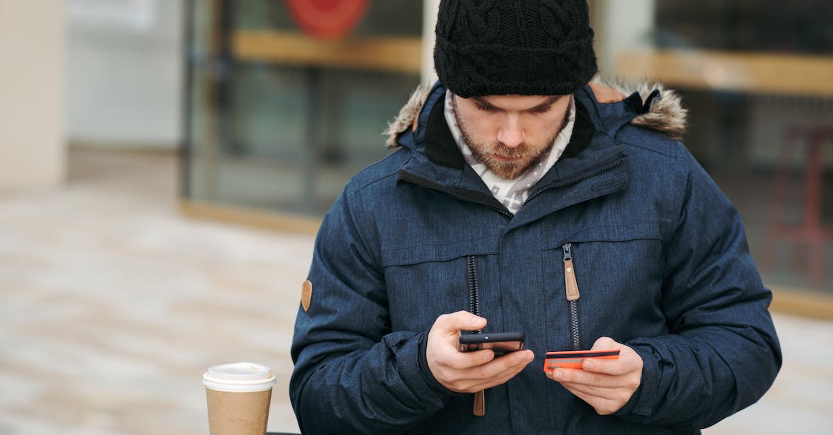 What to expect at a Global Entry application interview? - Focused male holding credit card while making payment with smartphone on street