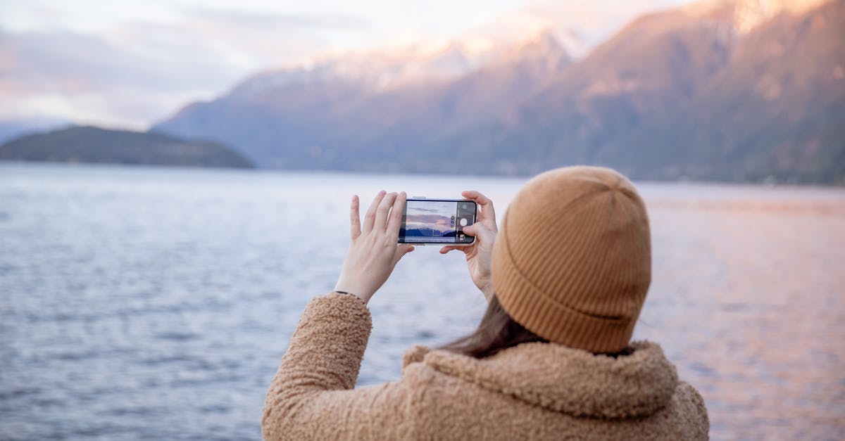 What warm clothes should I take when traveling in southeast Asia? [closed] - Back view of unrecognizable female tourist in warm coat and hat taking photo on smartphone while standing on coast near water and enjoying seascape during trip