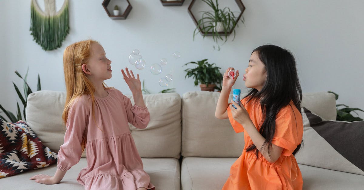 When is the best time to see live jazz in Europe? [closed] - Side view of cheerful little diverse girlfriends in trendy dresses sitting on comfortable sofa in cozy living room and blowing soap bubbles