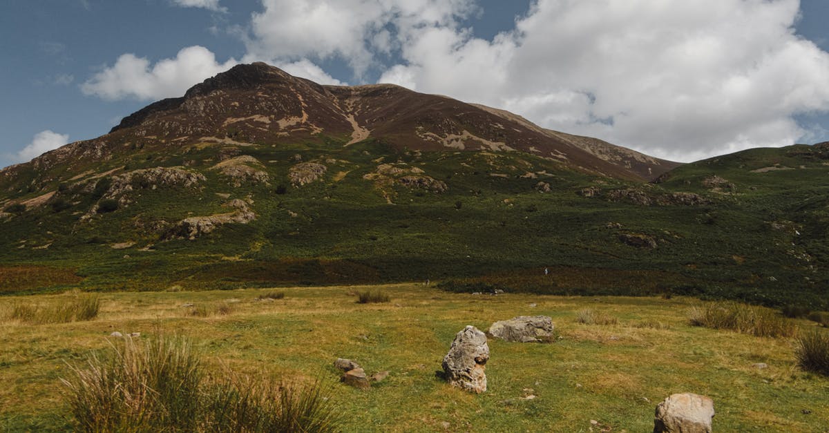Where's this verdant ridge? - Grassy valley with stones located near green hills against cloudy blue sky in nature Where's this verdant ridge? - Grassy valley with stones located near green hills against cloudy blue sky in nature