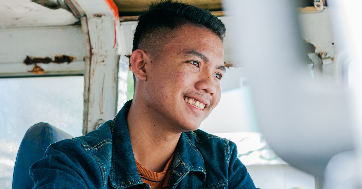 Where can a tourist to Malta ride an articulated bus? - Low angle of cheerful Asian male in denim shirt sitting in weathered public transport smiling away Where can a tourist to Malta ride an articulated bus? - Low angle of cheerful Asian male in denim shirt sitting in weathered public transport smiling away