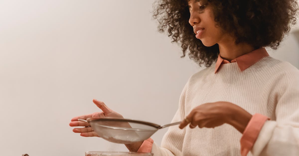 Where I can make chocolates in Switzerland - Side view of African American female cook with sieve pouring flour into bowl with chocolate batter while cooking in kitchen Where I can make chocolates in Switzerland - Side view of African American female cook with sieve pouring flour into bowl with chocolate batter while cooking in kitchen