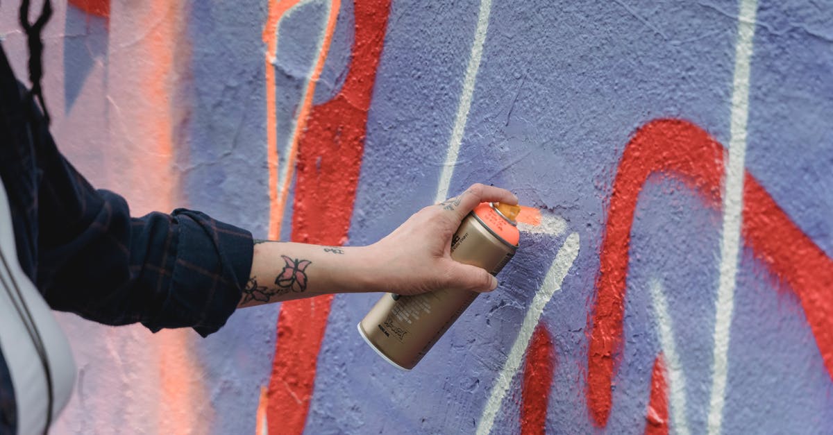Where in Amsterdam can one legally spray graffiti? - Crop unrecognizable painter with tattoos in black wear spraying orange paint on colorful purple wall with graffiti on street of city Where in Amsterdam can one legally spray graffiti? - Crop unrecognizable painter with tattoos in black wear spraying orange paint on colorful purple wall with graffiti on street of city