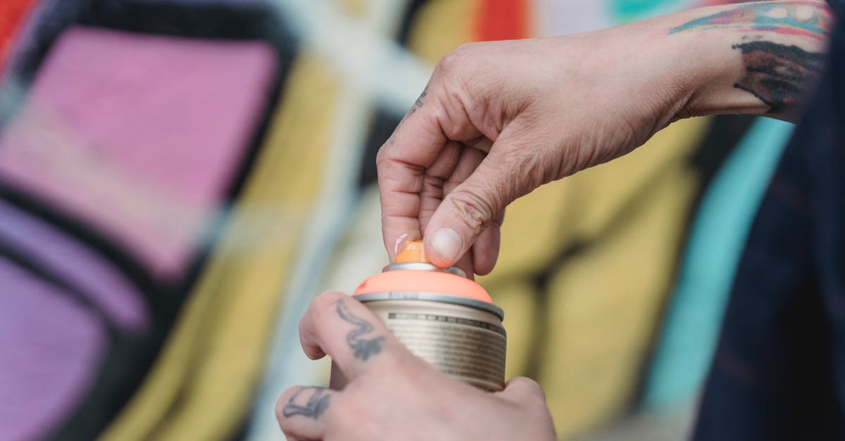 Where in Amsterdam can one legally spray graffiti? - Soft focus of crop unrecognizable painter with tattoos opening spray paint can while standing near colorful wall with creative graffiti Where in Amsterdam can one legally spray graffiti? - Soft focus of crop unrecognizable painter with tattoos opening spray paint can while standing near colorful wall with creative graffiti