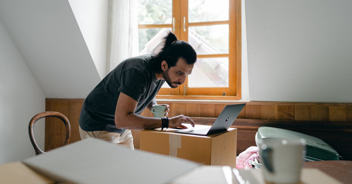 Where in Seoul can I rent a laptop? - Side view of focused bearded male in casual outfit with cup of hot drink browsing laptop while packing stuff into carton boxes Where in Seoul can I rent a laptop? - Side view of focused bearded male in casual outfit with cup of hot drink browsing laptop while packing stuff into carton boxes