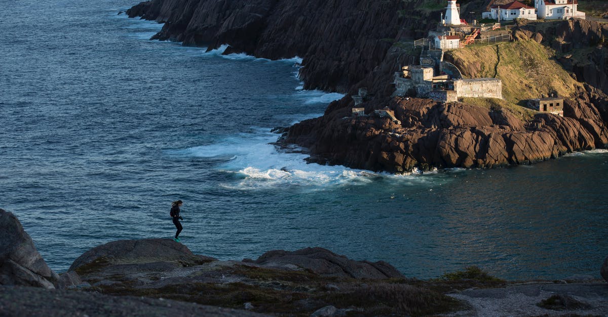 Where is this place "several houses on the rocky coast and rocky island with natural arch"? - Silhouette Photography of Person Standing on Cliff Where is this place "several houses on the rocky coast and rocky island with natural arch"? - Silhouette Photography of Person Standing on Cliff