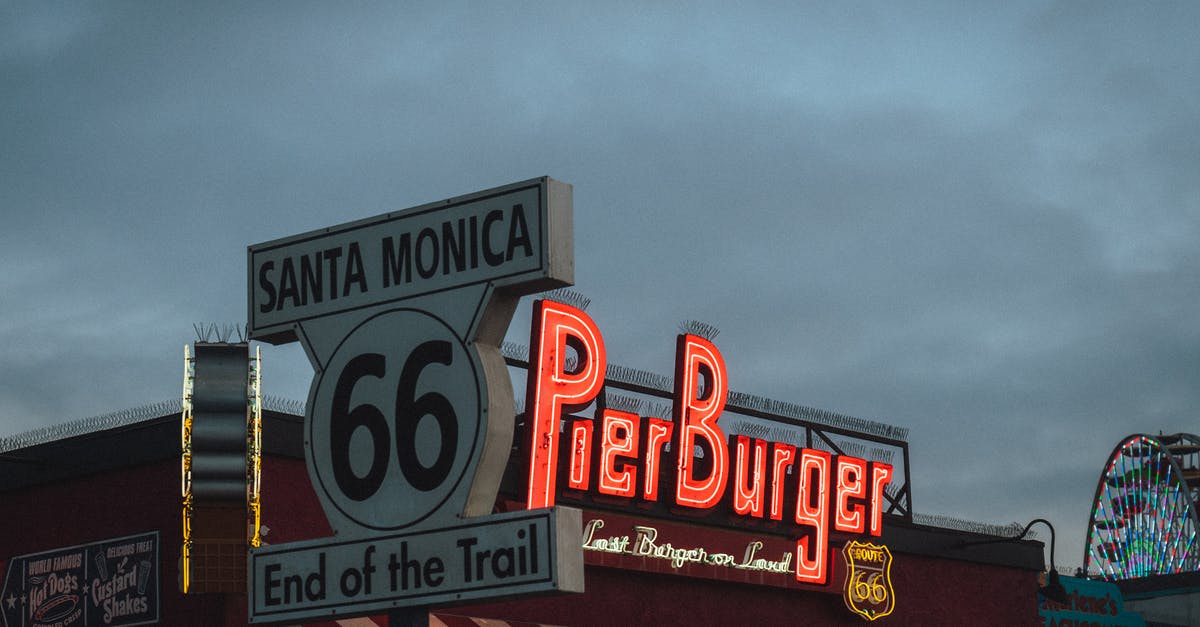 Where to buy a one-way travel insurance from the UK to the USA [closed] - Low angle of road sign with Route 66 End of the Trail inscription located near fast food restaurant against cloudy evening sky on Santa Monica Beach
