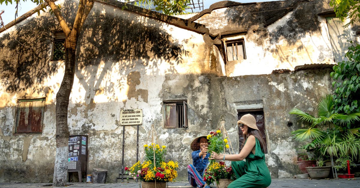 Where to buy a similar Vietnam SIM card aimed for locals/expats (not for tourists) in HCMC? [duplicate] - Side view of happy young ethnic female tourist in trendy clothes and hat sitting on haunches and buying bouquet of fresh flowers from local seller on town street