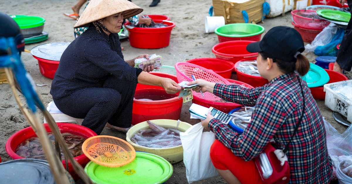 Where to buy a similar Vietnam SIM card aimed for locals/expats (not for tourists) in HCMC? [duplicate] - Asian female in traditional authentic Vietnamese hat sitting on stool in street fish market and selling seafood to female customer
