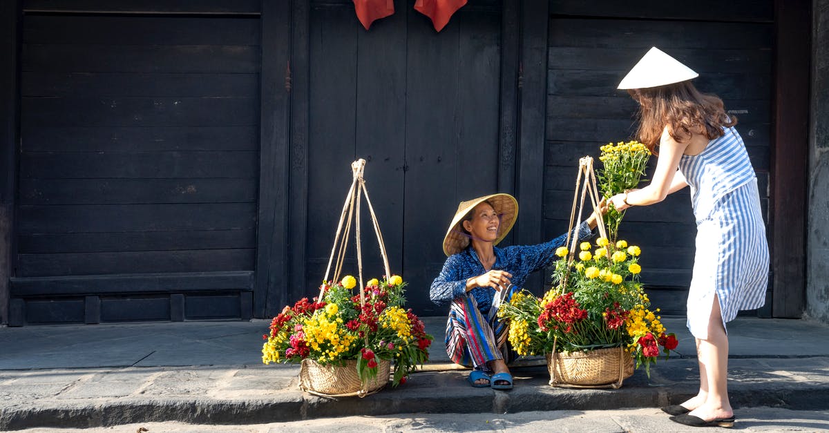 Where to buy a similar Vietnam SIM card aimed for locals/expats (not for tourists) in HCMC? [duplicate] - Side view of young stylish lady in dress and conical hat buying bouquet of flowers from ethnic happy female seller sitting on street on sunny day in town