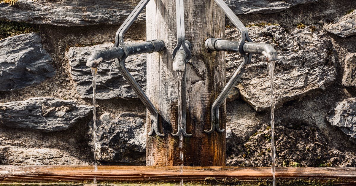 Where to find public water taps in the Netherlands? - Metal taps of fountain with pouring water into tank placed on wooden post near stone wall on street in city Where to find public water taps in the Netherlands? - Metal taps of fountain with pouring water into tank placed on wooden post near stone wall on street in city