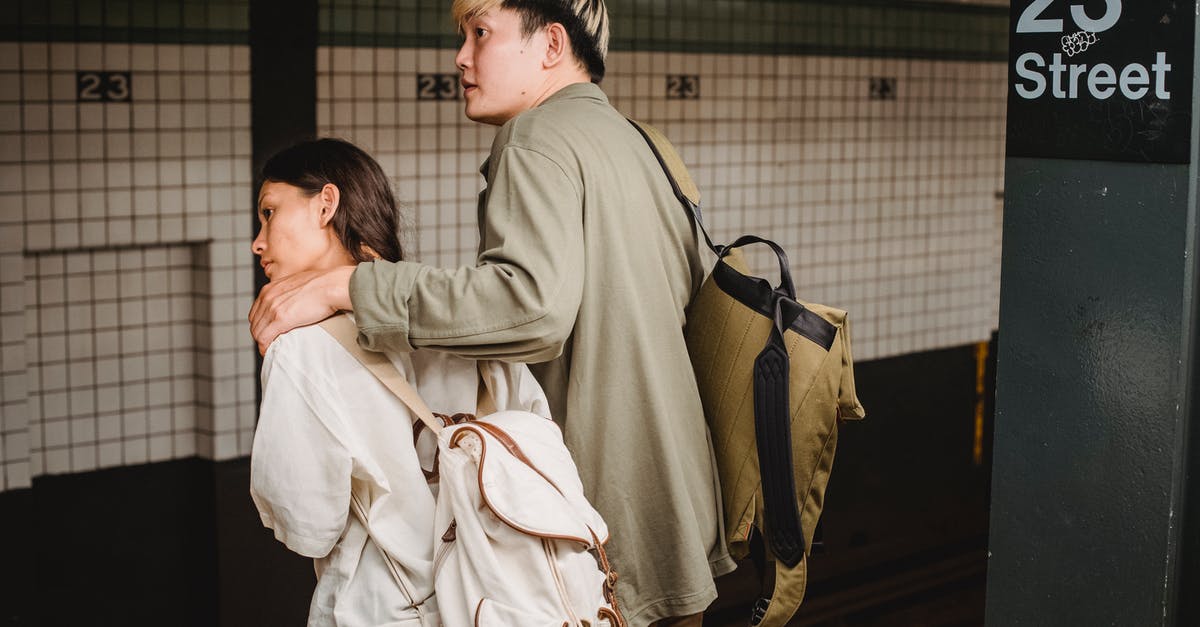 Where to meet travel partner at JFK (Terminal 4 arrivals) - Back view of Asian couple with backpacks hugging and standing on platform of subway station and leaning forward while waiting for train Where to meet travel partner at JFK (Terminal 4 arrivals) - Back view of Asian couple with backpacks hugging and standing on platform of subway station and leaning forward while waiting for train
