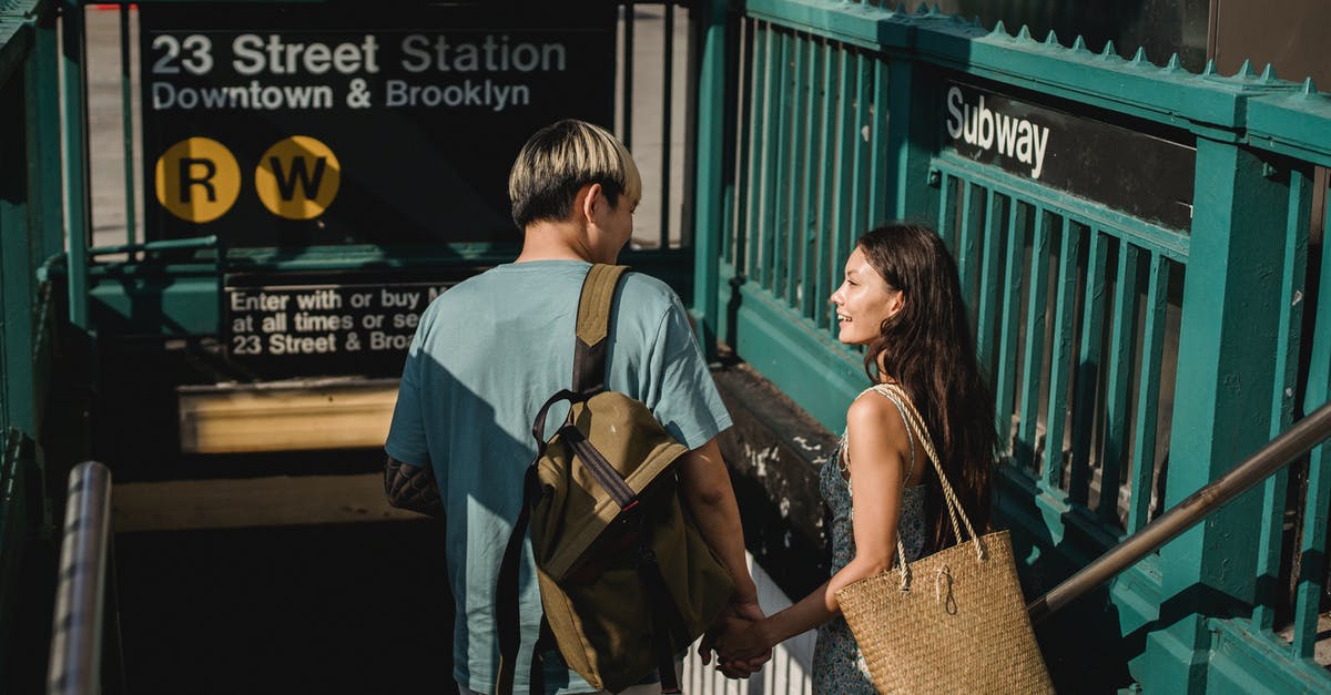 Where to meet travel partner at JFK (Terminal 4 arrivals) - Back view of young happy diverse couple with bags looking at each other near underground Where to meet travel partner at JFK (Terminal 4 arrivals) - Back view of young happy diverse couple with bags looking at each other near underground