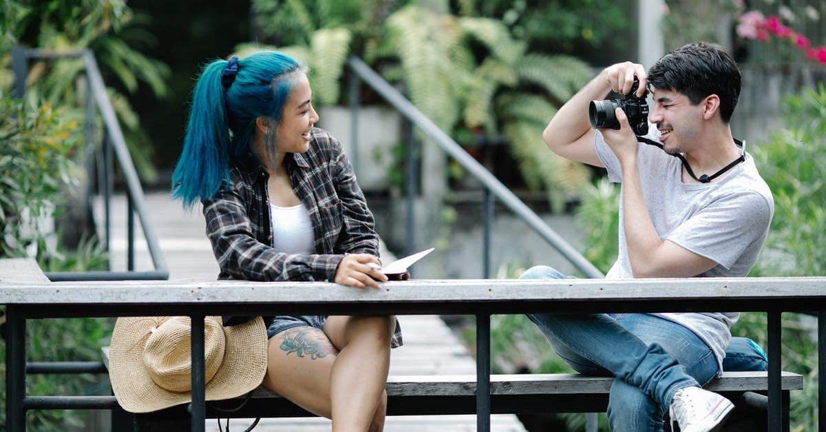Where was this photo of a bridge taken? [duplicate] - Positive young male photographer taking photo of female friend with blue hair and wearing checked shirt and shorts with tattoo on leg sitting on bench in suspension bridge in park