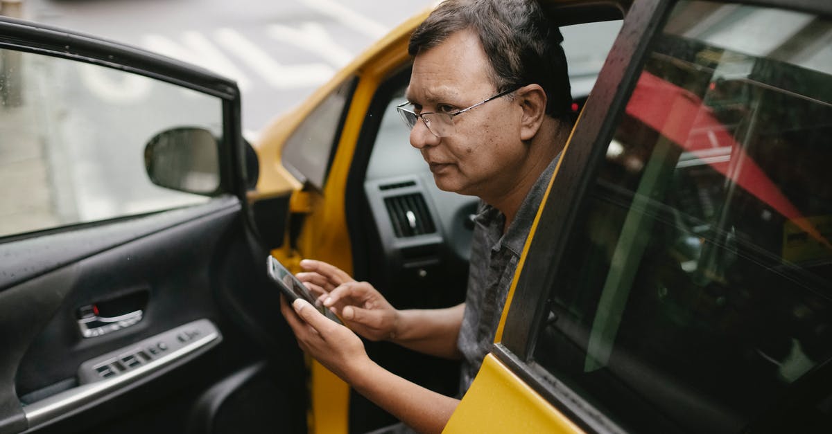 Which drivers license to use in the EU? - Crop Asian man sitting in parked yellow taxi car with open door and using smartphone while looking away Which drivers license to use in the EU? - Crop Asian man sitting in parked yellow taxi car with open door and using smartphone while looking away