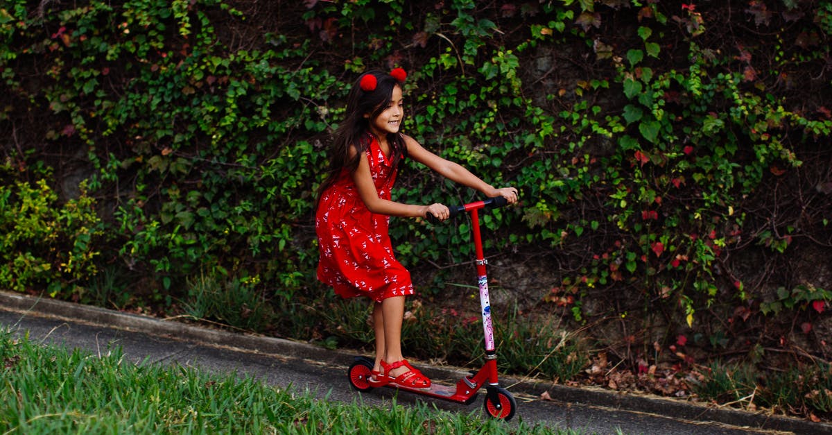 Which is faster for commuting, kick scooter or skateboard? [closed] - Side view of content child in dress riding kick scooter along road in park in summer
