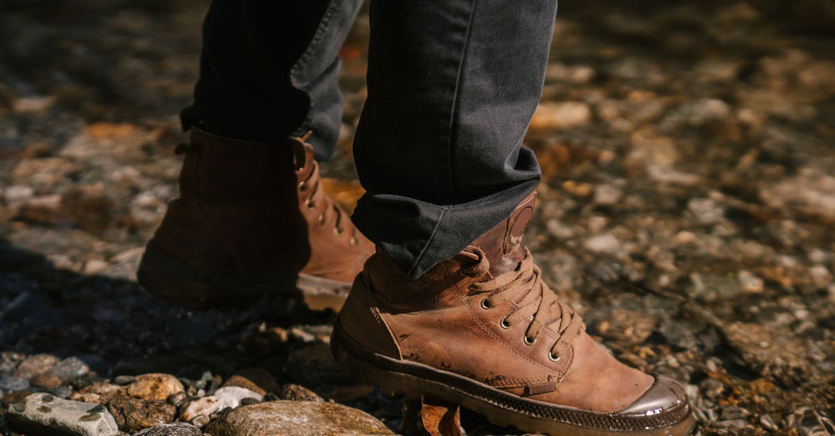 Which trekking shoes to get for trekking in Costa Rica - Crop anonymous person in brown boots and black jeans walking on stones near river bank Which trekking shoes to get for trekking in Costa Rica - Crop anonymous person in brown boots and black jeans walking on stones near river bank