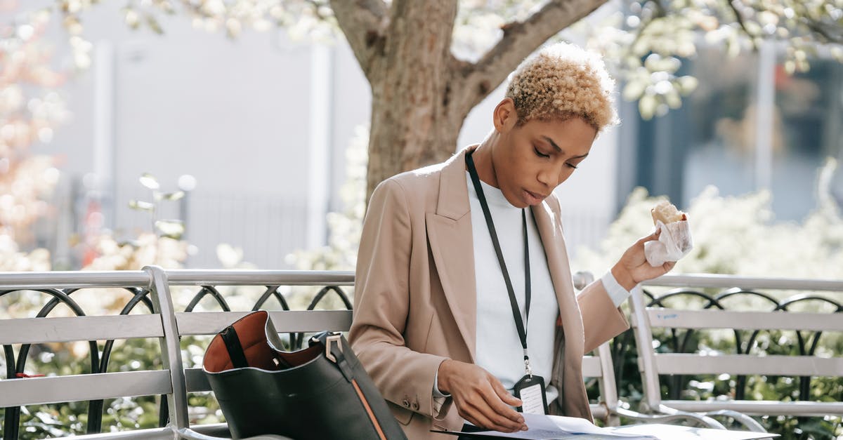 Which visa is applicable to me? Visitor or Short Student Study Visa - Pensive young African American female student in stylish jacket reading documents in folder and eating sandwich sitting in park