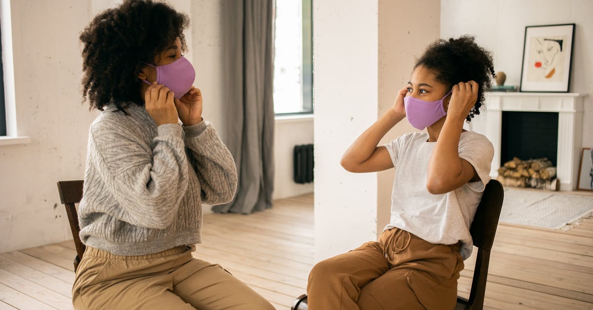 Why do flight attendants say in safety instructions that you should put on your own mask before helping others? - Side view of African American mother and daughter wearing protective masks looking at each other while sitting in room with fireplace during coronavirus pandemic