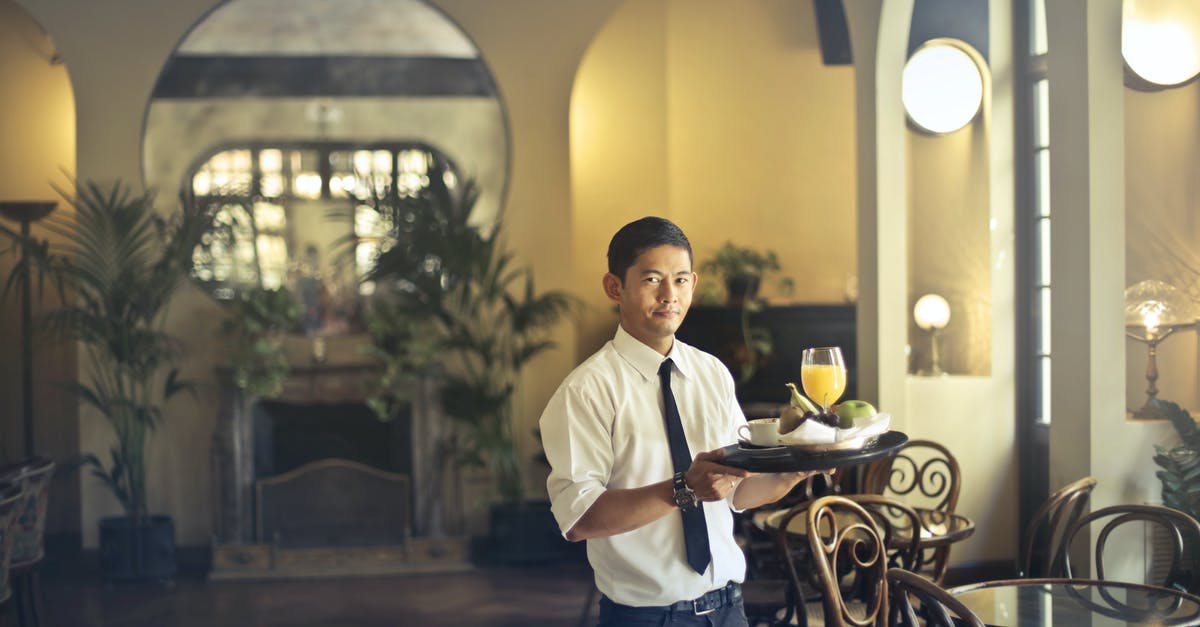 Why do hotels (apparently) require you to leave and then ask for your room key back at the reception when leaving/returning to the hotel? [duplicate] - Confident young ethnic waiter in elegant clothes holding tray with food and drinks and looking at camera while serving tables in stylish restaurant