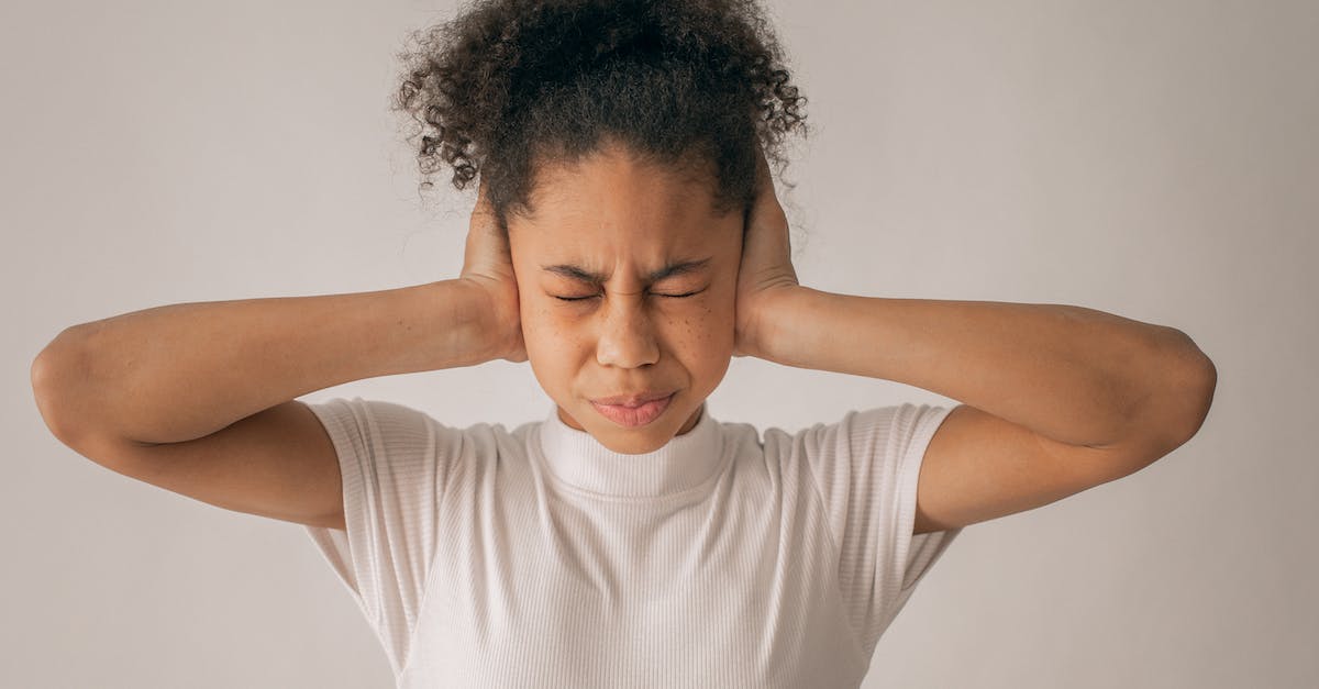 Why do I feel pressure in the ears in a plane? - Despaired African American teenage girl with black hair and closed eyes covering ears while standing on white background in light studio Why do I feel pressure in the ears in a plane? - Despaired African American teenage girl with black hair and closed eyes covering ears while standing on white background in light studio