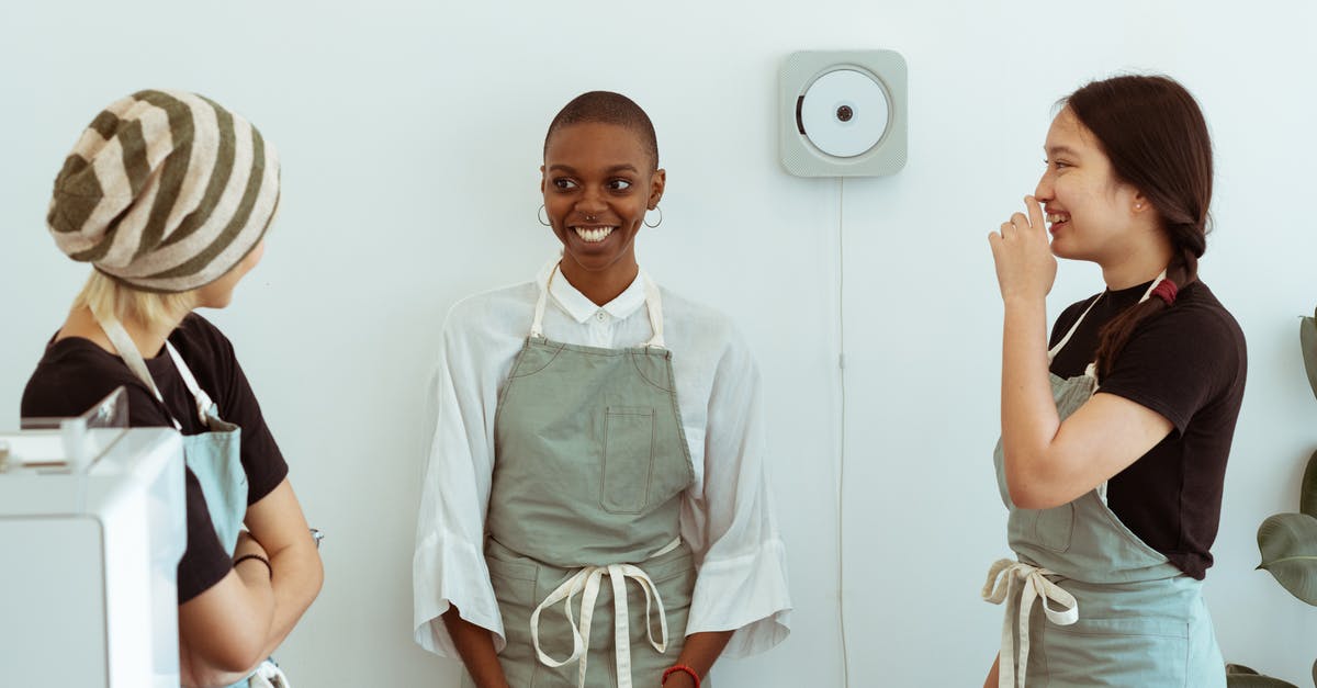 Why do immigration officers ask to see ID other than your passport? - Positive young diverse female baristas in apron uniforms communicating with shy newcomer during break at work