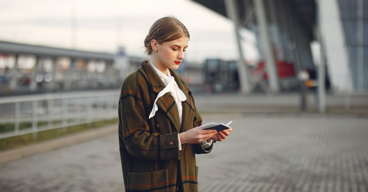 Why does immigration check passports at some Schengen-only terminals? - Attentive female passenger wearing trendy plaid coat and white blouse checking passport and ticket standing on pavement near modern building of airport outside