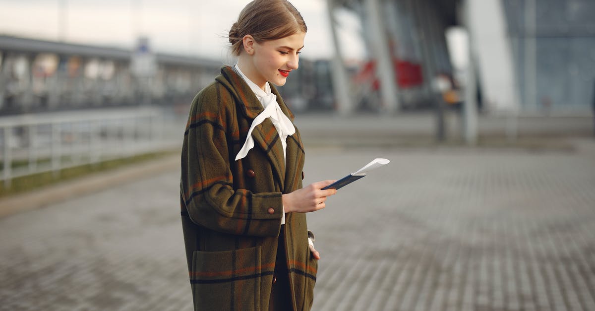 Why does immigration check passports at some Schengen-only terminals? - Smiling female passenger wearing trendy plaid coat and white blouse checking passport and ticket standing on pavement near contemporary building of airport