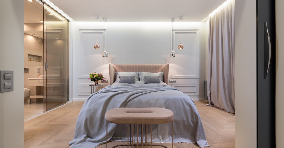 Why don't American hotels have ceiling lights? - Interior of modern light home with bed with pillows and blanket next to table under lamps near pouf and glass door to washroom Why don't American hotels have ceiling lights? - Interior of modern light home with bed with pillows and blanket next to table under lamps near pouf and glass door to washroom