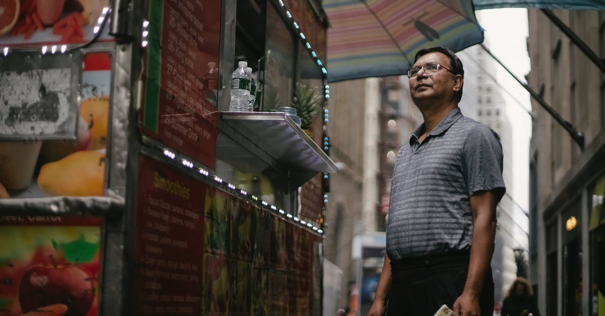 Why would I choose full service carrier instead of a low-cost one? - Low angle of pensive male in glasses and casual clothes standing near truck with street food and choosing meal