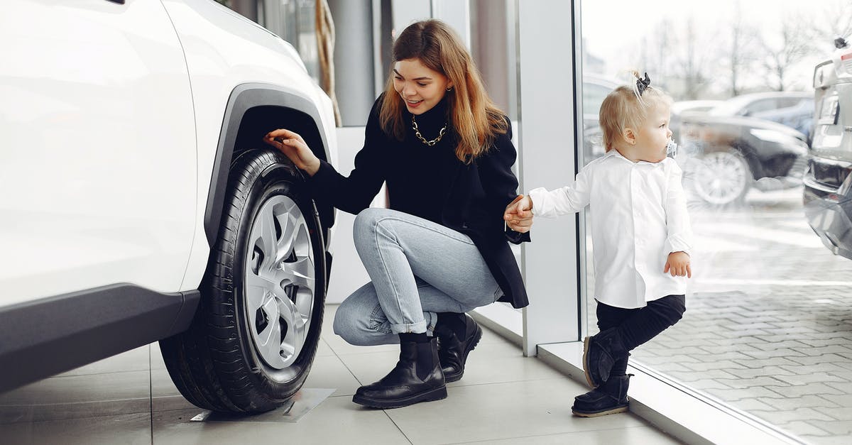 Why would I choose full service carrier instead of a low-cost one? - Full length of cheerful smiling mother in jeans holding hands with cute little girl and looking at car wheel in car showroom in daylight