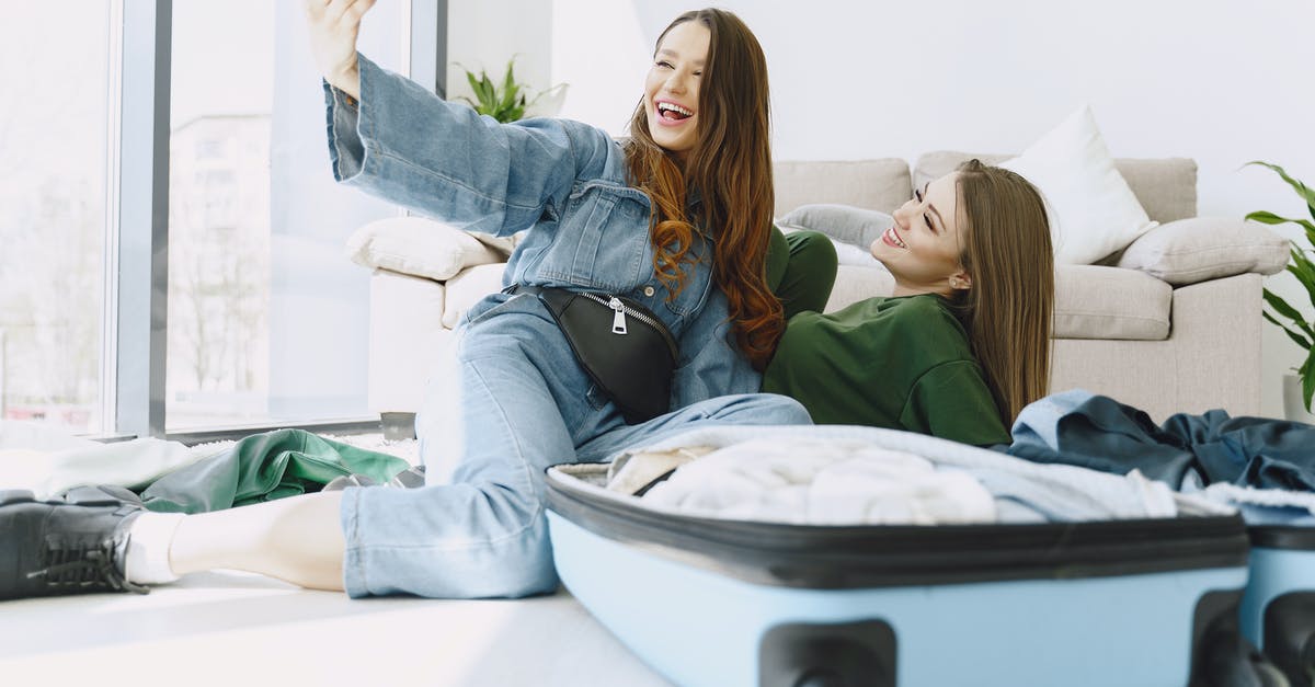 Will I have to get my luggage in Houston or it will be delivered to Tucson? - Happy young female friends in trendy outfits having fun and taking selfie while packing suitcase in cozy room Will I have to get my luggage in Houston or it will be delivered to Tucson? - Happy young female friends in trendy outfits having fun and taking selfie while packing suitcase in cozy room