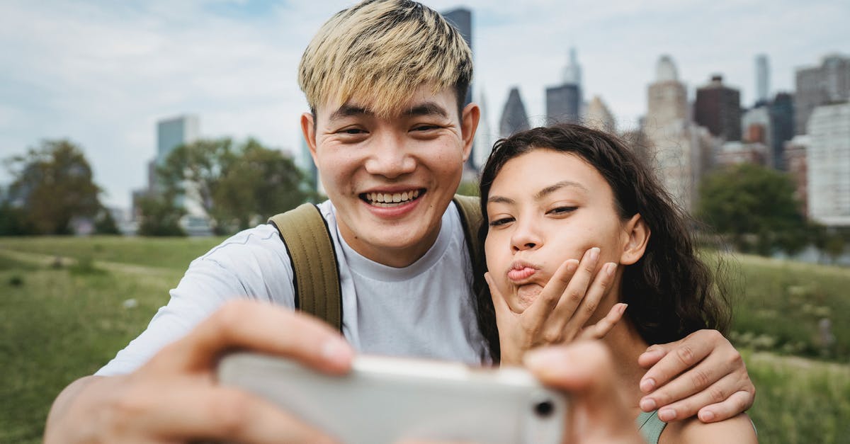 Will we have enough time to make our connecting flight at Heathrow? - Cheerful Asian boyfriend hugging ethnic girlfriend making grimace while taking self portrait on cellphone in green city park Will we have enough time to make our connecting flight at Heathrow? - Cheerful Asian boyfriend hugging ethnic girlfriend making grimace while taking self portrait on cellphone in green city park
