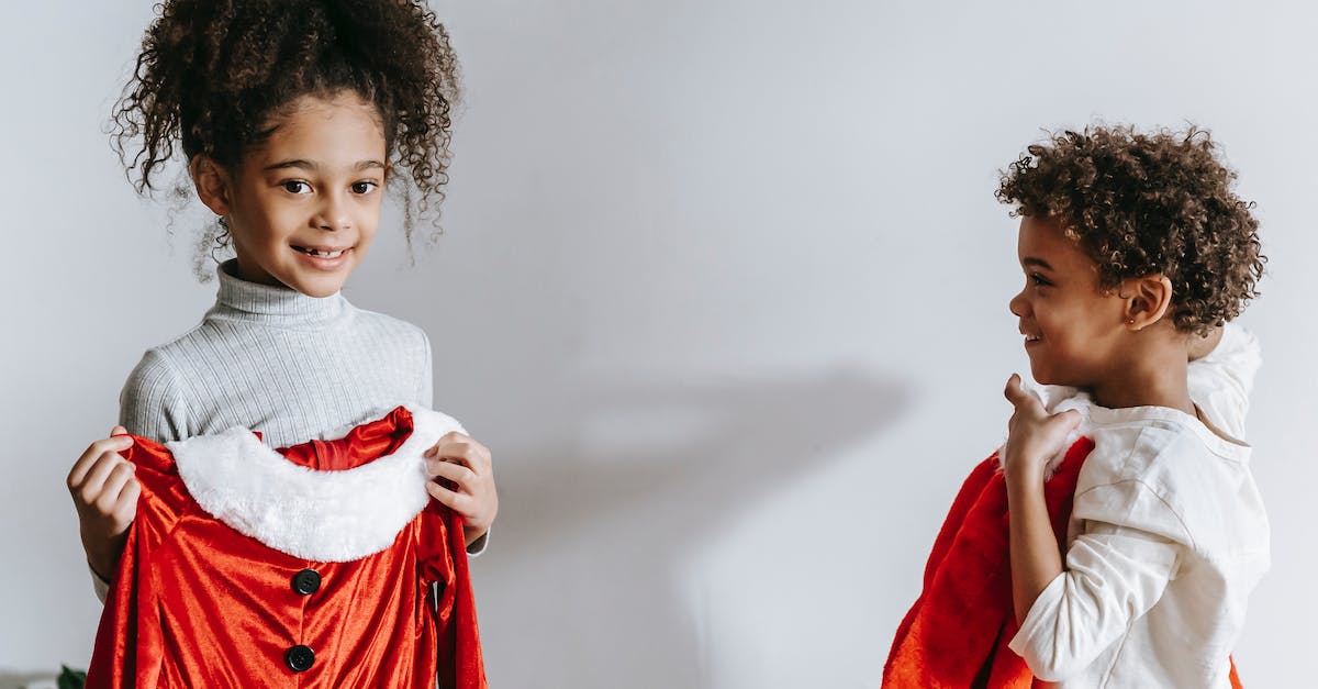 Winter apparel for Europe (November-December) - Cheerful African American siblings with red Santa Claus outfits in hands standing in light room at home during Christmas holiday Winter apparel for Europe (November-December) - Cheerful African American siblings with red Santa Claus outfits in hands standing in light room at home during Christmas holiday