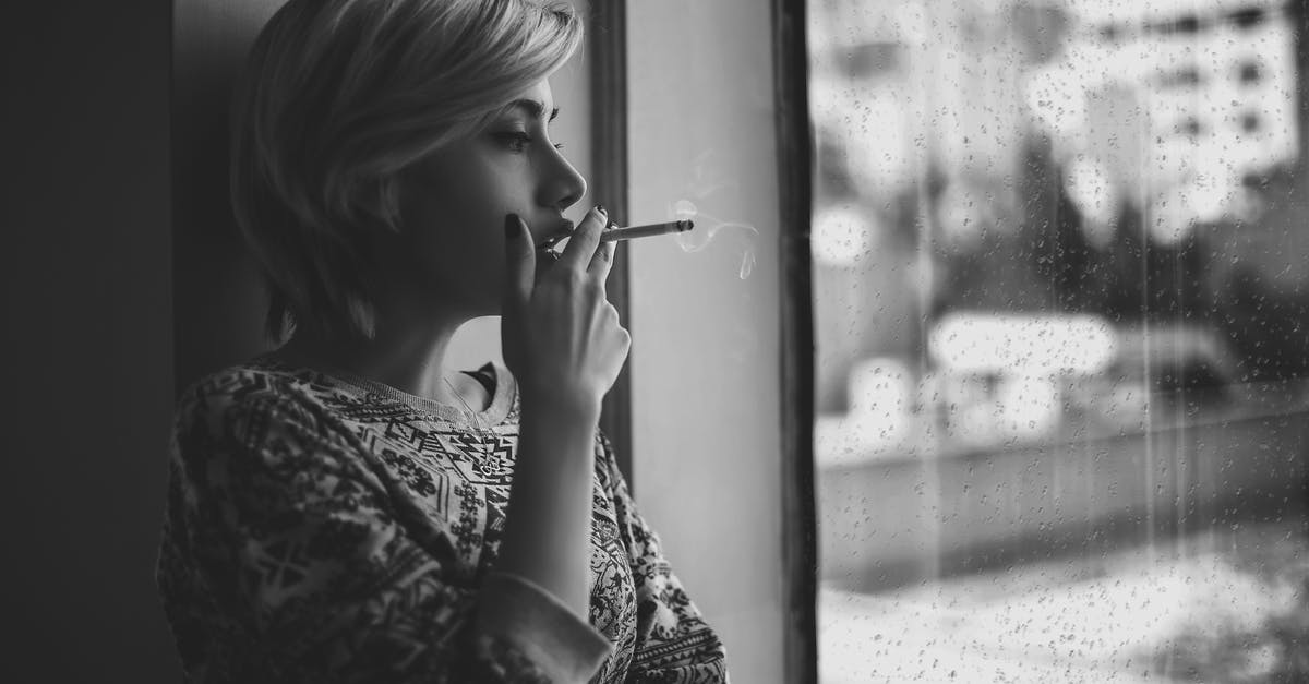Worried about short layovers - Black and white depressed female with short haircut smoking cigarette and looking out window at rainy city Worried about short layovers - Black and white depressed female with short haircut smoking cigarette and looking out window at rainy city