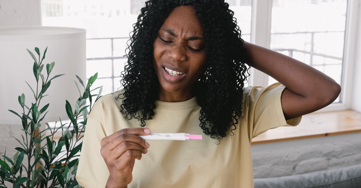 Worried that my parents information might not match - Frustrated African American female in casual clothes looking at pregnancy test in hand while standing in light living room at home